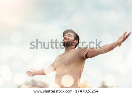 Happy Traveler male embracing life and enjoying freedom with open arms over sky and bokeh effect. Carefree smiling Bearded man standing relaxing and breathing fresh nature air