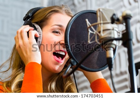 Young female singer or musician with microphone and headphone for audio recording in the Studio