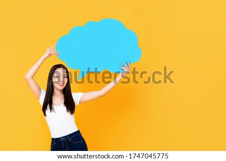 Beautiful Asian woman smiling and holding empty speech bubble isolated on yellow background