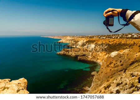 A camera in men's hands photographs the beautiful landscape of the Crimea. Sea rocky coast with capes. Blue sky and blue sea.
