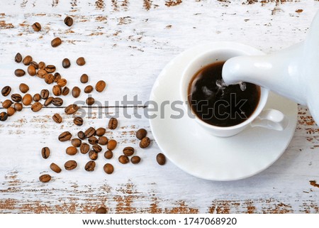 Hot tasty coffee in cup with coffee beans on wooden background