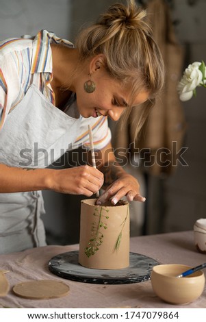 Beautiful girl making clay vase. Young female clay designer using special handtool to cut out shapes from soft stuff while working over new item. Handcraft product.