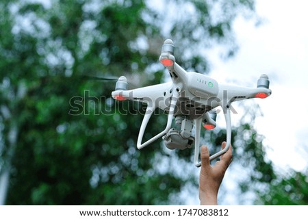 Hand reaching for a white drone with camera flying in summer