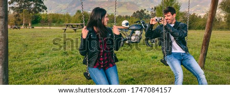 Young man taking a picture of his girlfriend sitting on the swings in a recreational area