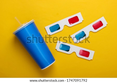 Movie time. Stereoscopic anaglyph disposable paper 3d glasses, paper cup of drink on yellow background. Top view