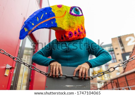 Masked woman - brightly colored bird head with a large beak. homemade original costume for the holiday. woman depicts a bird.