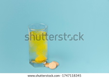 A glass of water and pills on a blue background close-up. A tablet of vitamins is dissolved in water. Copy space.