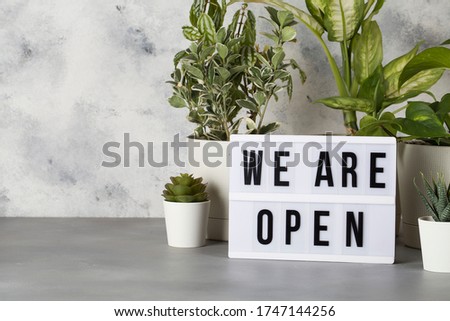 light box with text WE ARE OPEN among the plants in pots , reopening after covid-19 shutdown concept copy space
