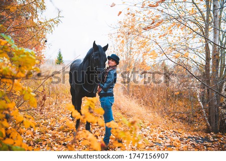 girl next to a black horse on the background of autumn nature