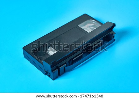 Single black old plastic vhs video cassette lies on blue desk. Concept of 90s. Close-up