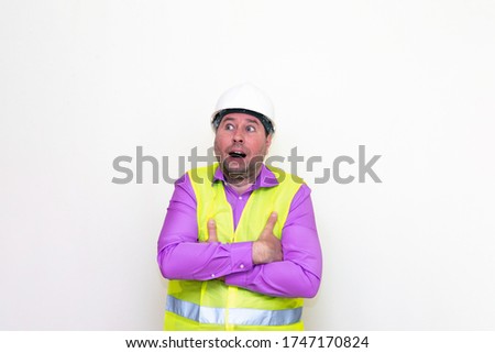 Curious caucasian engineer looking a side crossed his arms about himself on a white wall.Copy space.