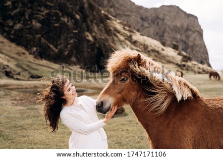 Destination Iceland wedding photo session with Icelandic horses. A bride in a white dress strokes a horse's nose. Hair and mane develop in the wind.