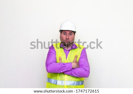 Curious strange caucasian engineer looking at camera crossed his arms about himself on a white wall.Copy space.