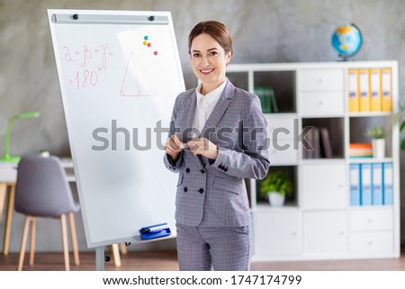 Photo of pretty teacher lady home study online lesson listen video call students new theorem rule knowledge stand white board wear plaid suit formalwear living room house classroom indoors
