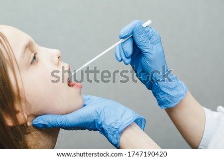 Pediatrician taking saliva test sample from elementary age girl's mouth performing Saliva testing (Salivaomics) diagnostic procedure Royalty-Free Stock Photo #1747190420