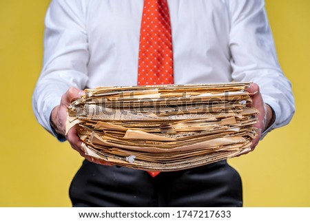 Studio shot of businessman or accountant holding pile of papers. Yellow background
