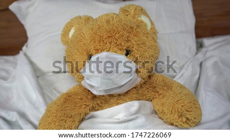 A teddy bear lies in bed in a medical mask. The bear got sick.