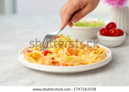 Hand with fork tasting Italian pasta fettuccine with shrimps in white bowl on gray table. Close up beautiful picture homemade national cuisine. Home Cooking