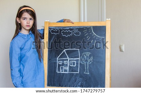 the girl drew a house and the sun with chalk on the Board, so she learns to draw