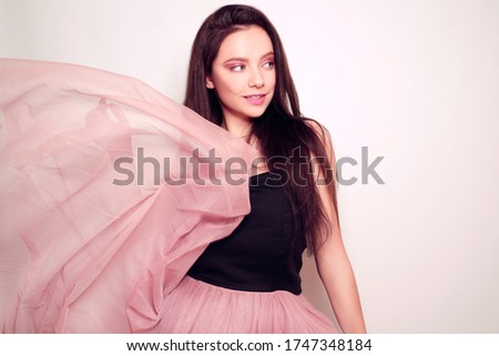 Beauty brunette girl with long hair. Model in a pink dress, flying dress, fabric. Pink makeup, style, fashion, beauty photo.