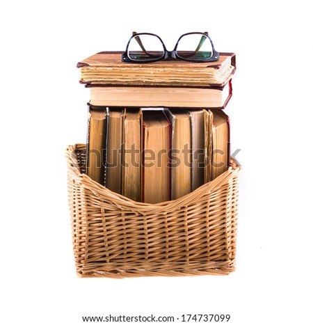 Stack of old antique books in a wicker basket and spectacles lying on top, isolated on white background.