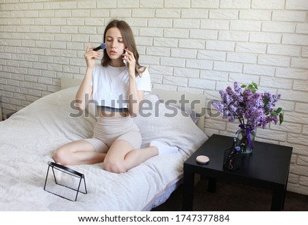 Beautiful women using phone and doing make up on her bed at home.