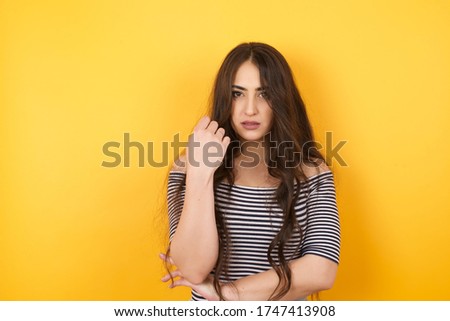 Isolated portrait of stylish European woman with hand near face and looking to the camera with doubtful and skeptical expression suspect and doubt. Isolated over yellow background.