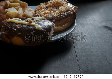 Three donuts with chocolate on top on a white plate on a rustic table lit by window light, dark food photography or low key light concept, desserts with chocolate, sweet food 