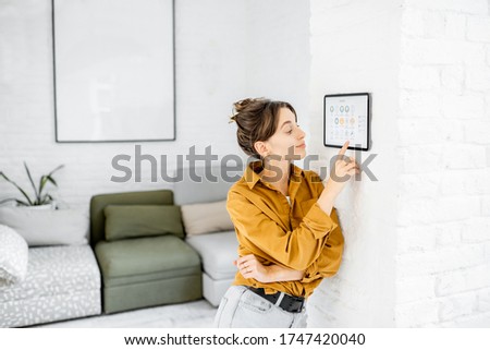 Woman controlling home with a digital touch screen panel installed on the wall in the living room
