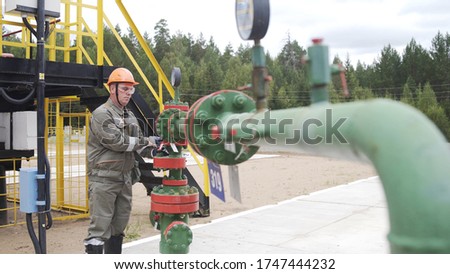 Oilman in orange helmet and protective glass opening or closing valve of wellhead. Injection tree is destined for injection wells sealing and their operating regime regulation. Oil industry