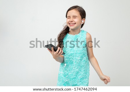 charming teen girl listens to music in headphones with her eyes closed holding a smartphone in her hand on a white background