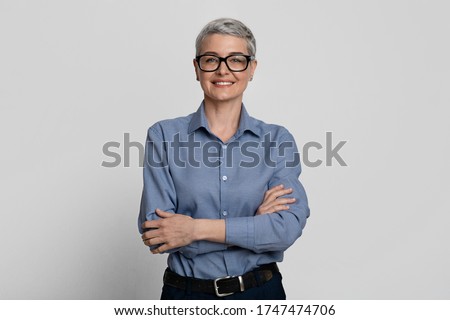 Female Entrepreneurship. Portrait Of Attractive Mature Businesswoman In Eyeglasses Posing With Folded Arms Over Light Background In Studio, Copy Space