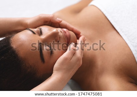 Closeup of therapist hands making facial massage for young black lady at spa salon Royalty-Free Stock Photo #1747475081