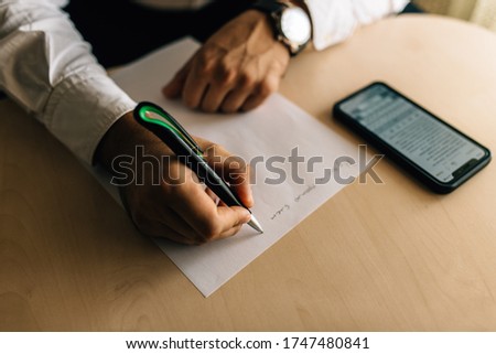 
Men's style. The guy writes a letter on a piece of paper with a pen. Nearby on the table is a telephone.