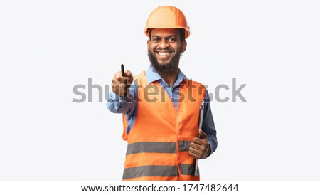 African Construction Workman Giving Instructions Pointing At Camera Holding Pen Standing On White Studio Background. Panorama Royalty-Free Stock Photo #1747482644
