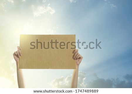 Woman's hands holding a blank banner to put the text at protesting with clear sky and sunlight background.
