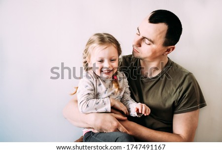  Blurred young dad plays with his daughter in his arms in the room on the bed. The girl laughs and dad looks at her with love. Relations between father and daughter.