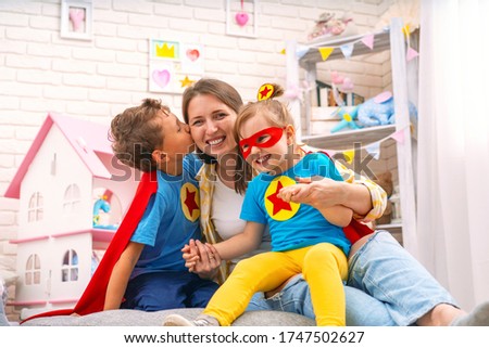 happy woman plays superhero games with her children in nursery. brother and sister, dressed in superhero costumes, laugh happily. Mom and kids love spending time together. son kisses his mother.