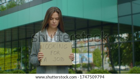 Left to right pan real time portrait shot of businesswoman standing near office center with a sign "looking for job".