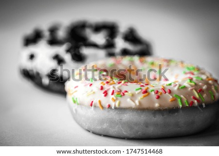 Close-up on ring donut with white glaze and colourful hundreds and thousands, black and white image with selected colour