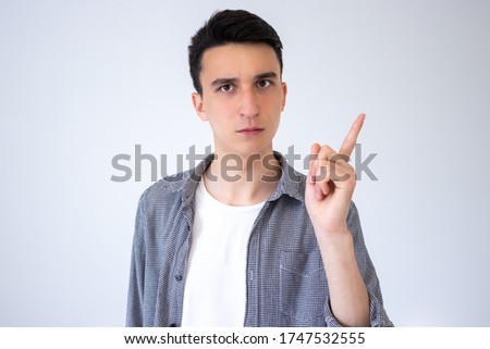A strict and dissatisfied guy waves his index finger. The guy's reaction to some misdemeanor. Guy on a gray background.