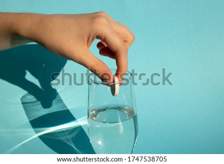 Against a blue background, a hand drops a dissolving fizzy aspirin tablet into a glass of water