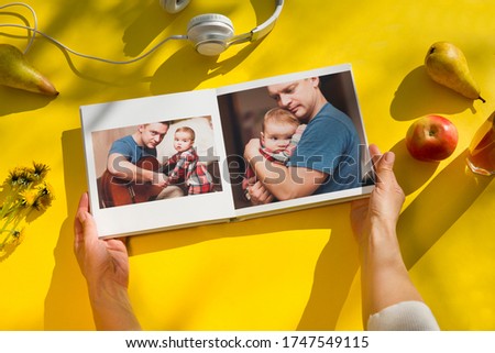 woman hands holding a family photo album agains on a yellow background. summertime. flat lay
