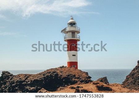 Part of the red and white lighthouse by the ocean.