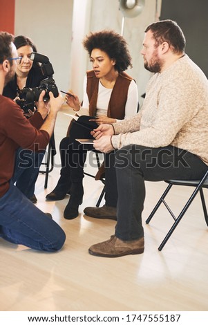 Young handsome bearded educator showing to his multicultural attendees how camera works. Photo studio interior.