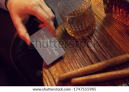 Man's hand puts exclusive membership card on the table. Gentleman's hand puts exclusive membership card on the wooden table with whisky in carafe and glass with cigars. Royalty-Free Stock Photo #1747555985