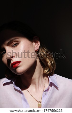 Fashion side portrait of attractive young woman standing against dark background wearing lavender shirt. Vertical shot.