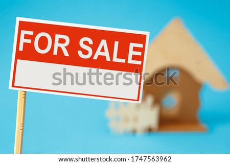 A sign for the sale of real estate and a house in the background. Real estate sale concept