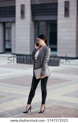 Full-length vertical photo of a business girl standing on the street in the city center and talking on the phone.