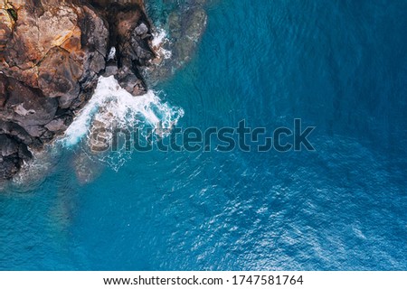 Top aerial view of turquoise Atlantic ocean water waves crashing on rocks on the Portuguese Madera island seashore.